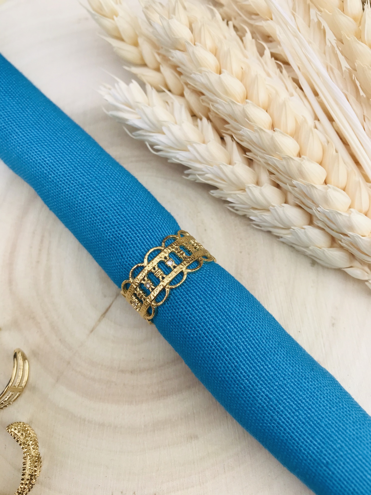 Guardanapo azul com argola dourada e trigo seco sobre madeira