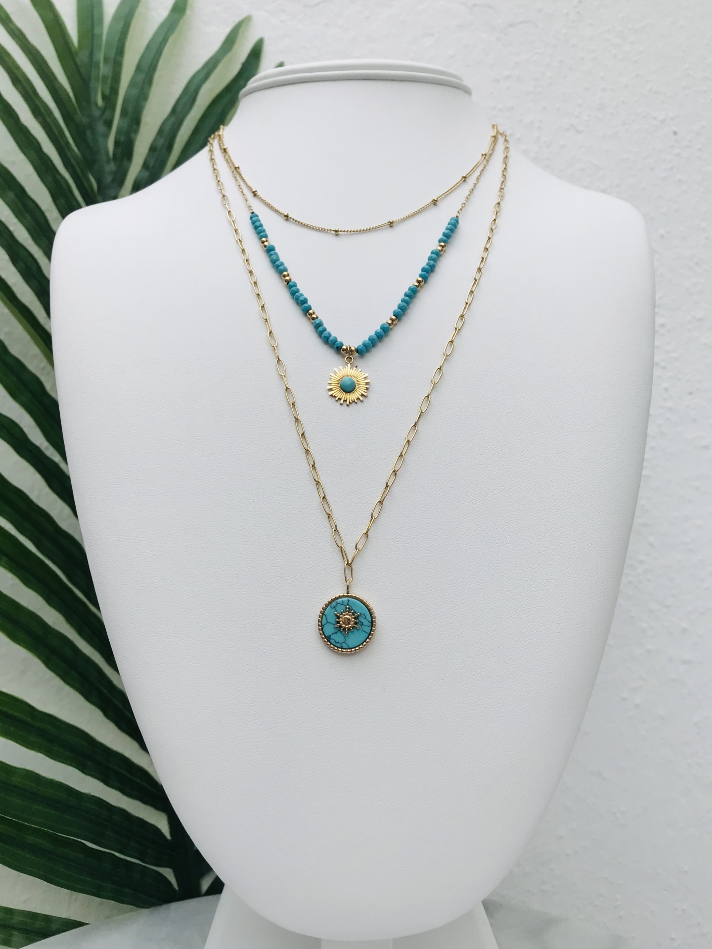 Colar triplo dourado com detalhes azul-turquesa exibido em busto branco