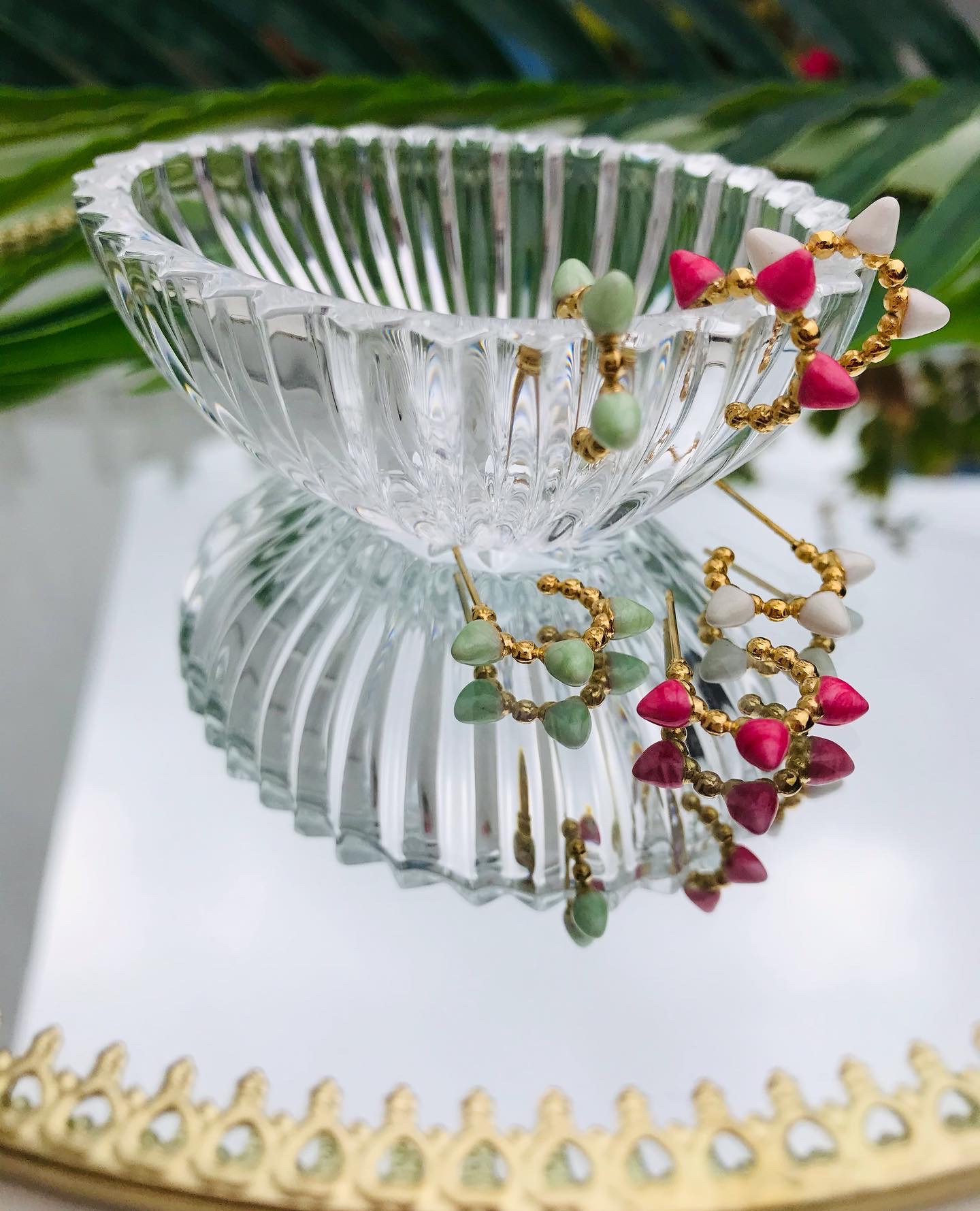 Brincos de argola coloridos sobre taça de vidro e espelho com moldura dourada