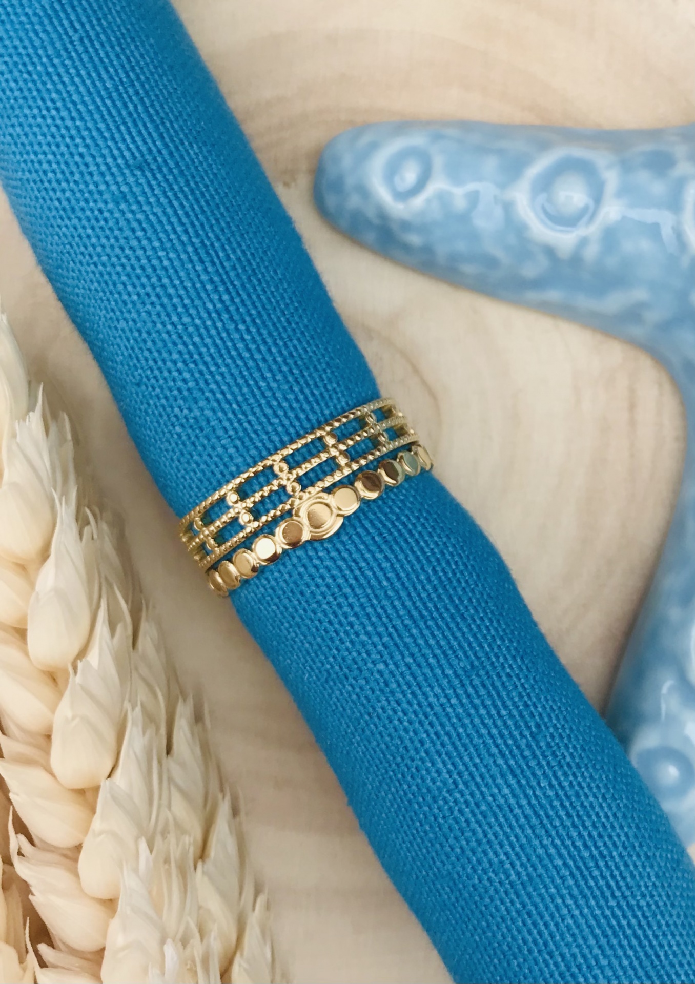 Anel dourado com três bandas distintas em tecido azul e fundo com espigas e decoração azul