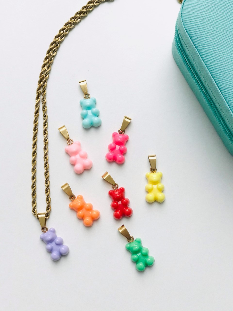 Colar dourado com pendente ursinho lilás e vários pendentes coloridos ao lado sobre fundo branco