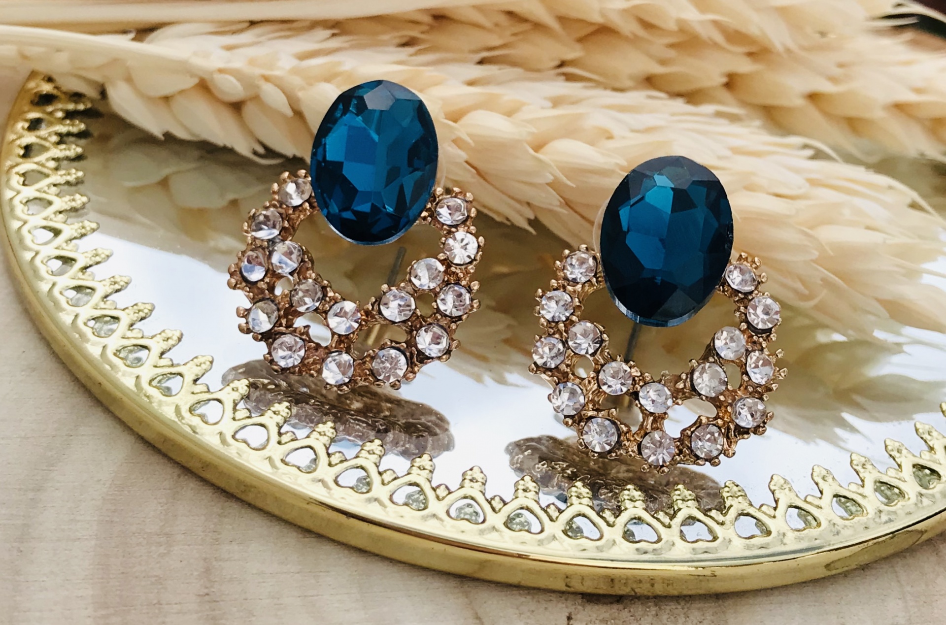 Brincos azul e pedras transparentes num espelho redondo com moldura dourada