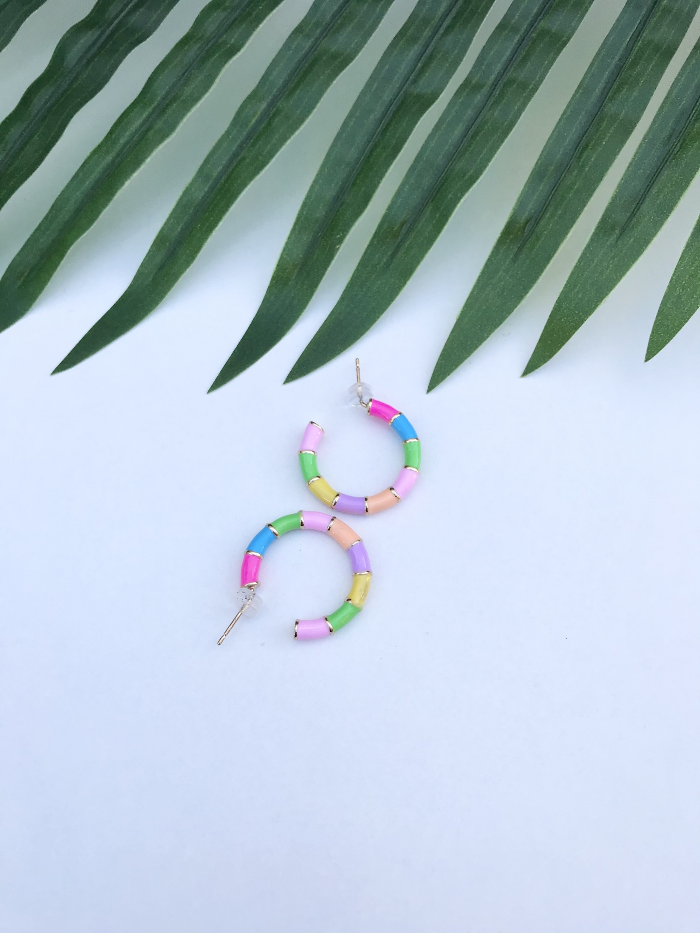 Brincos coloridos em forma de argola sobre fundo branco com folhas verdes