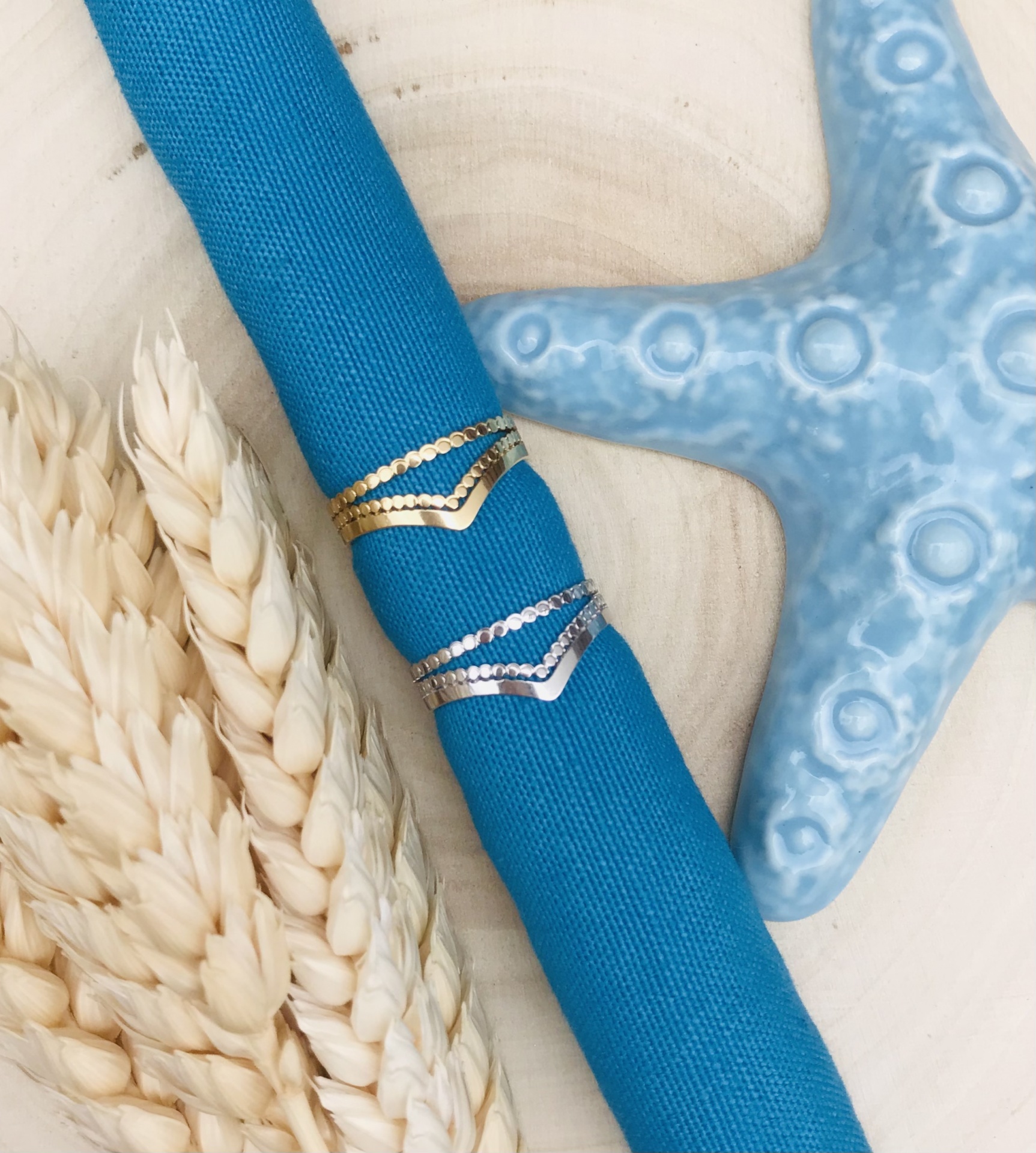 Anéis dourado e prateado sobre tecido azul com estrela-do-mar e espigas de trigo ao lado