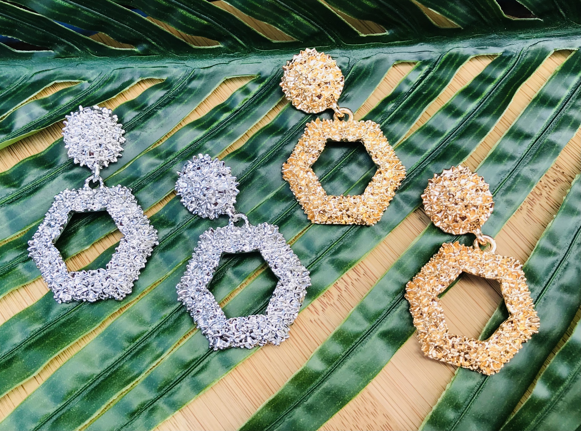 Brincos hexagonais texturizados prateado e dourado sobre folha verde