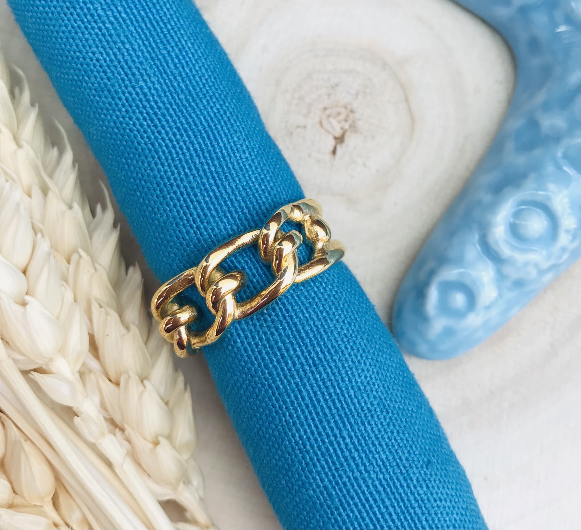 Anel dourado de elos grossos em tecido azul com elementos naturais e figura azul