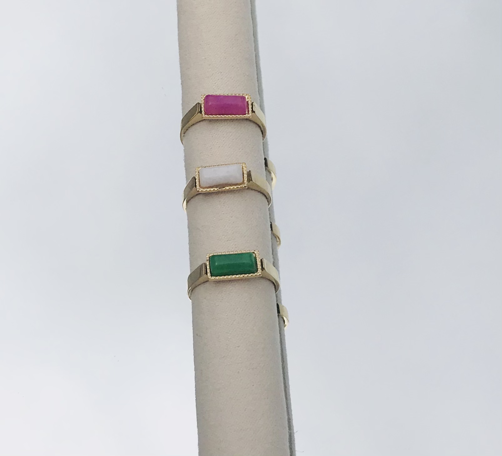 Três anéis dourados com pedras coloridas em suporte cilíndrico creme