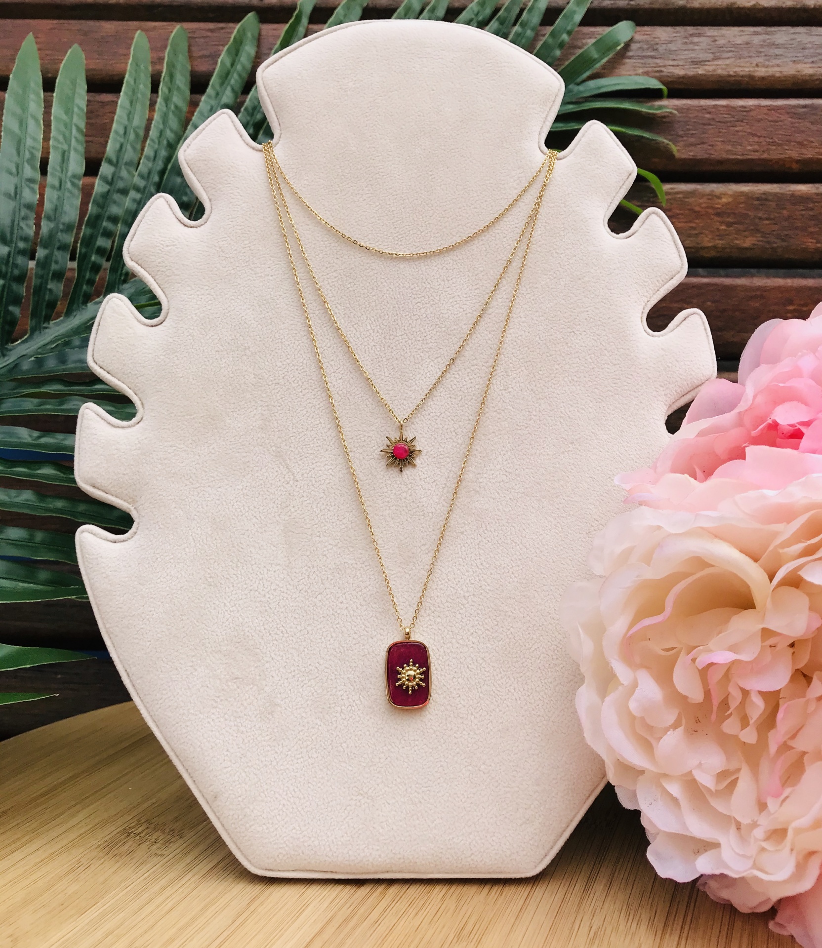 Colar duplo dourado com pendentes vermelhos exibido em suporte branco em forma de folha