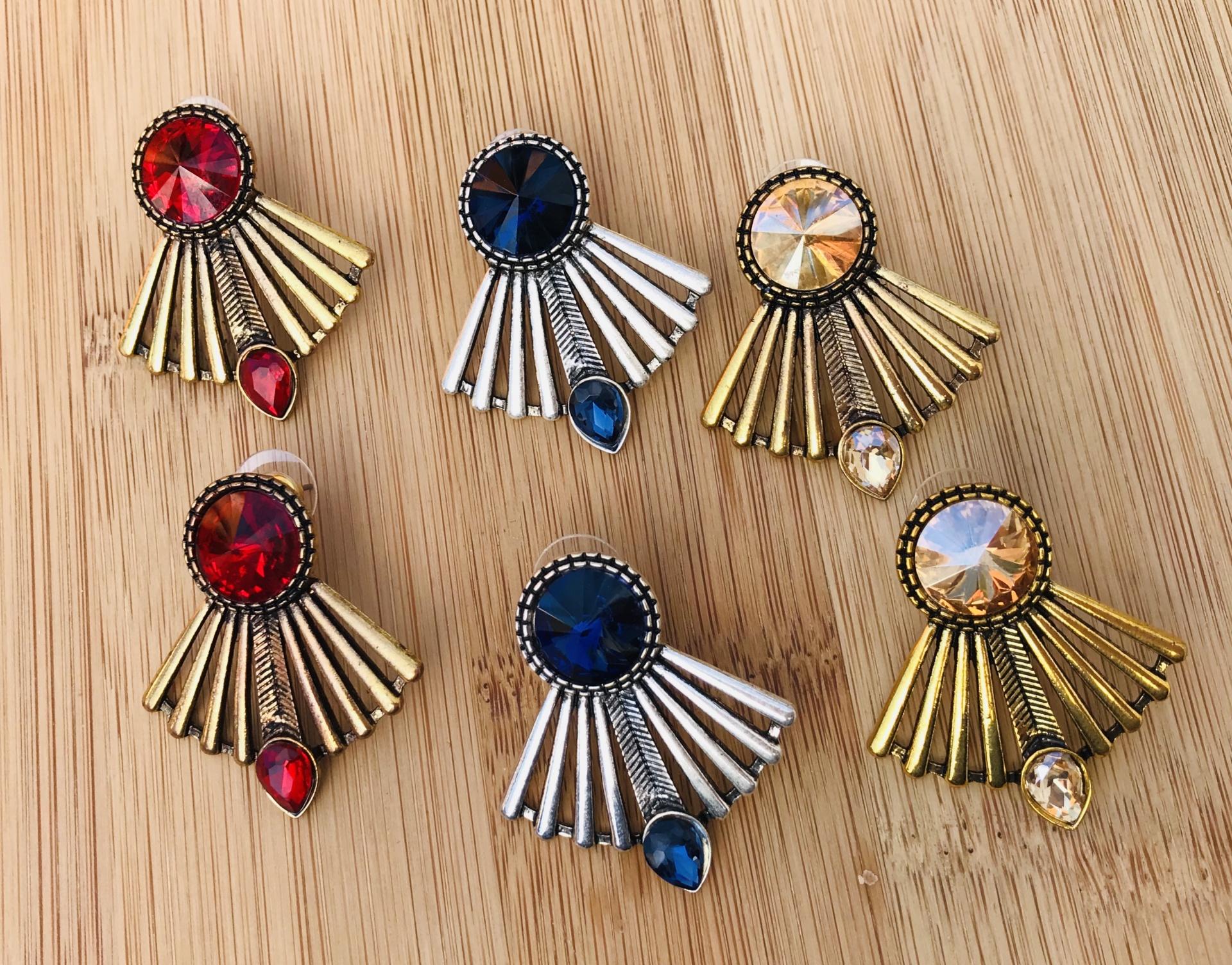 Brincos coloridos com pedras e elementos metálicos sobre madeira clara