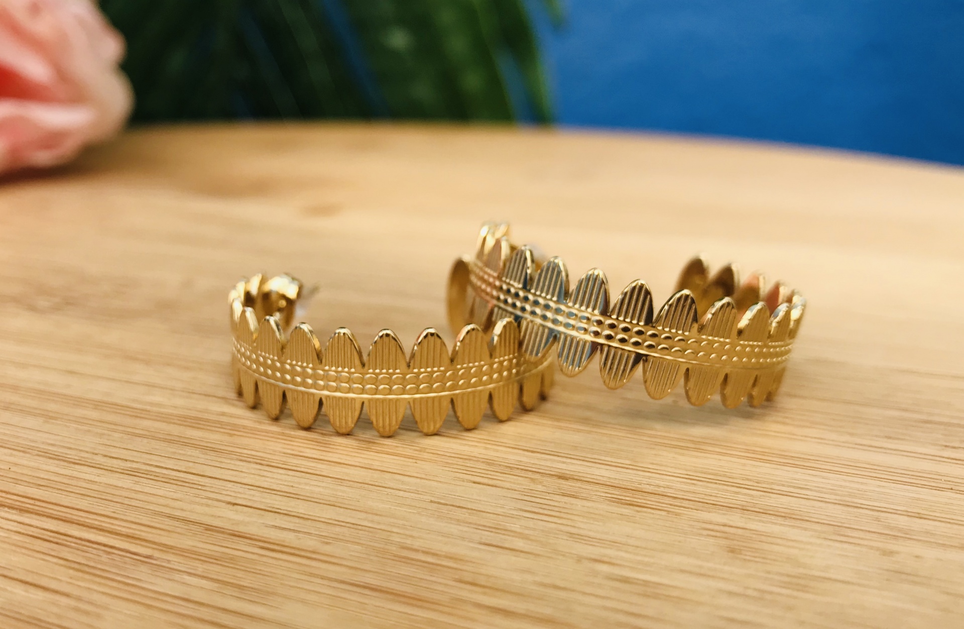 Duas pulseiras douradas com padrão de folhas sobre madeira clara