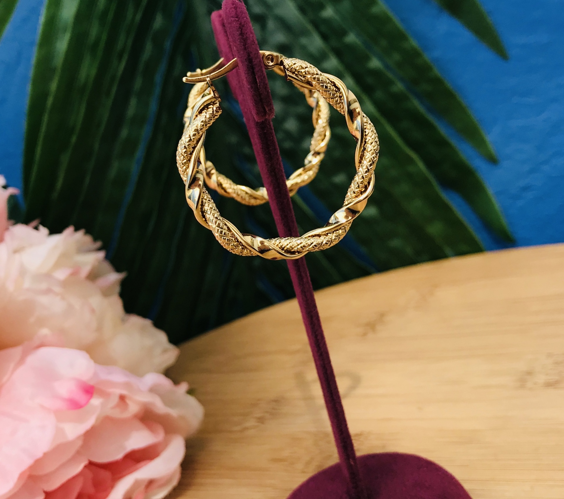 Brincos argola dourados texturizados expostos em suporte de veludo vermelho em fundo colorido