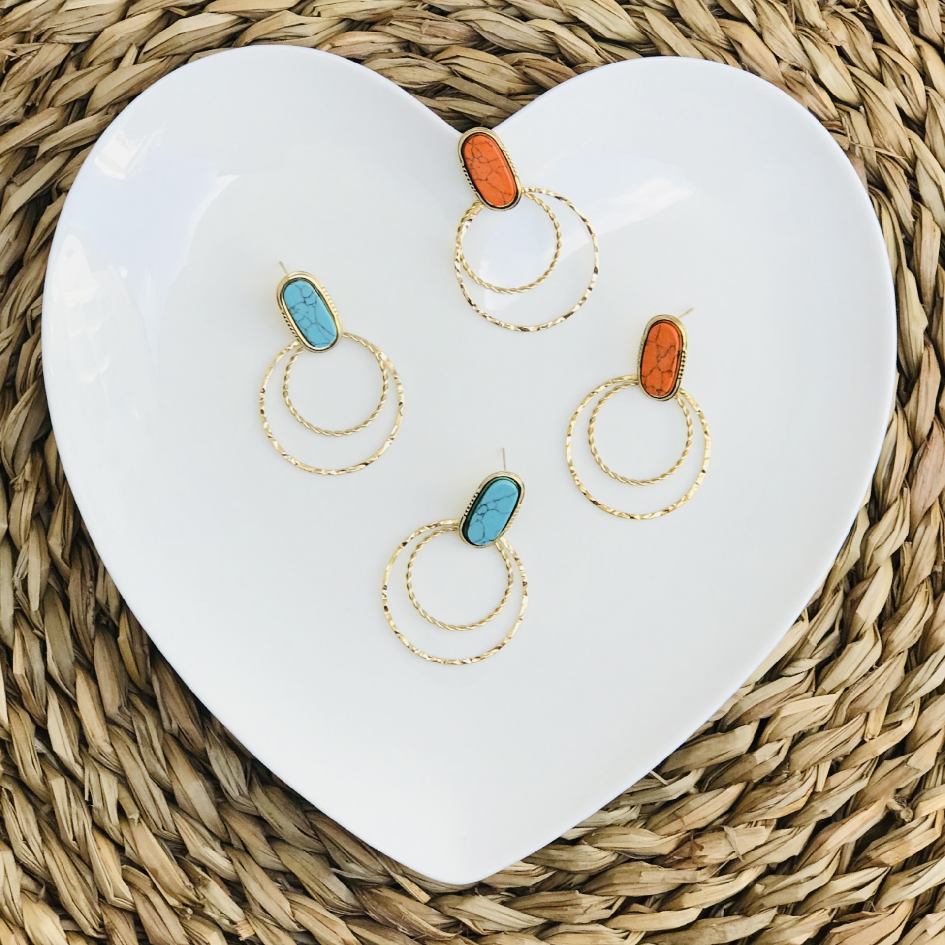 Brincos de argola dupla dourada com pedra turquesa e laranja em prato branco de coração