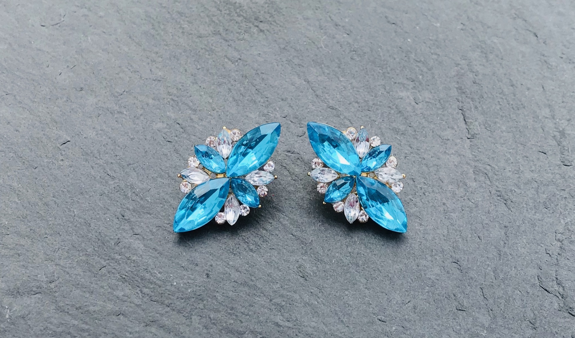 Par de brincos com pedras azuis e brancas sobre superfície cinza rugosa