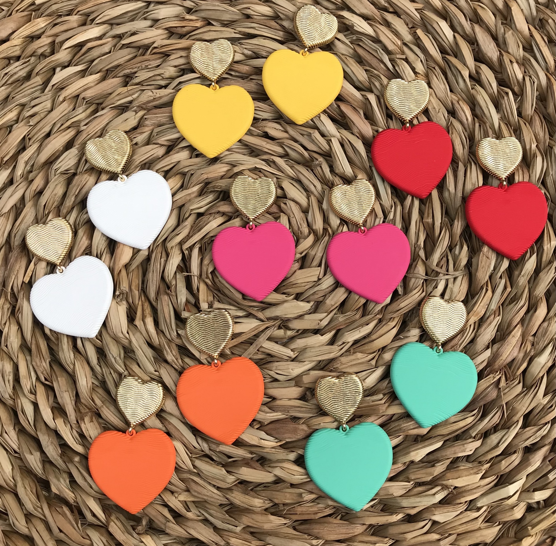 Brincos coloridos em forma de corações com detalhes dourados sobre superfície trançada