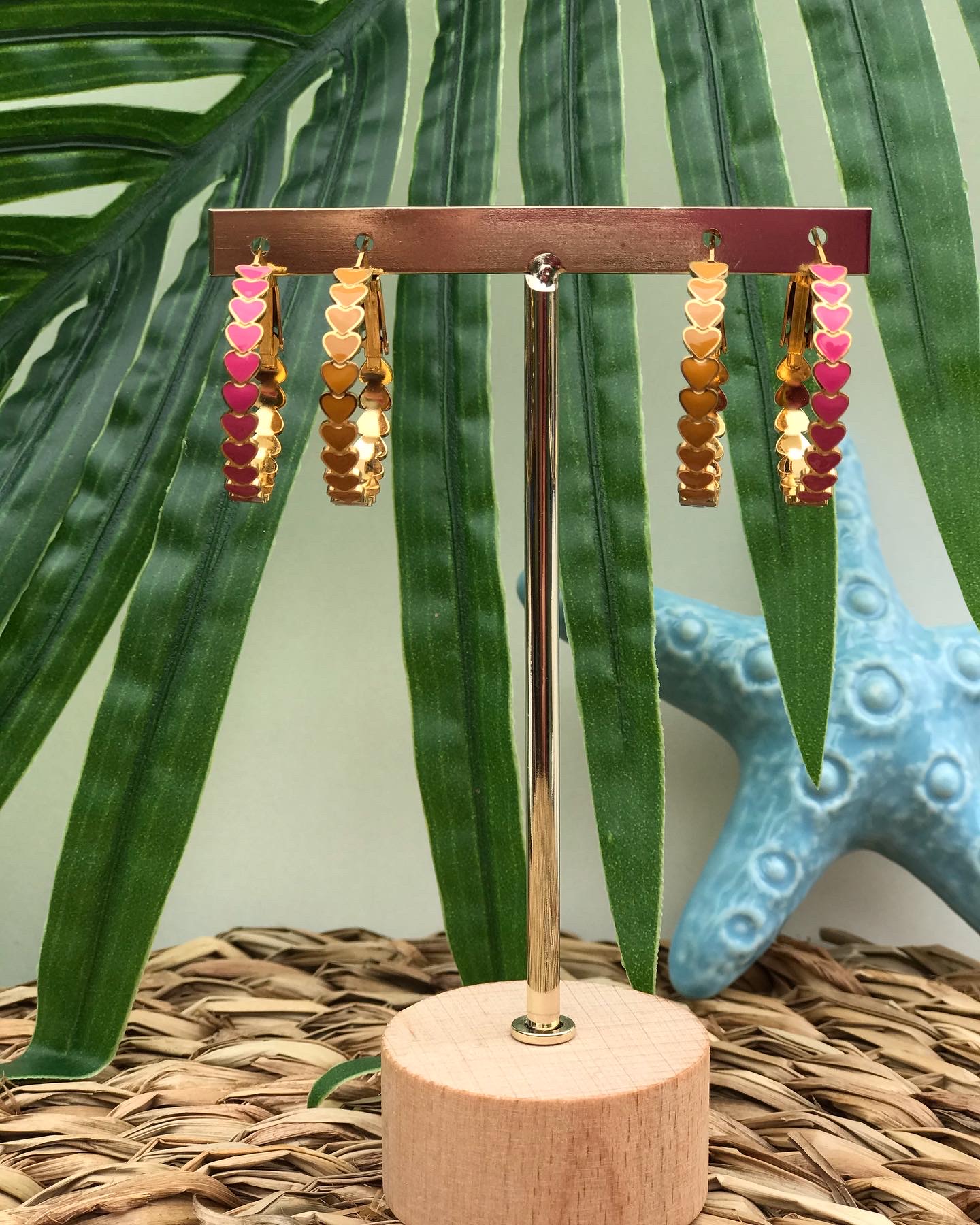 Brincos de argola dourados com corações coloridos pendurados em suporte