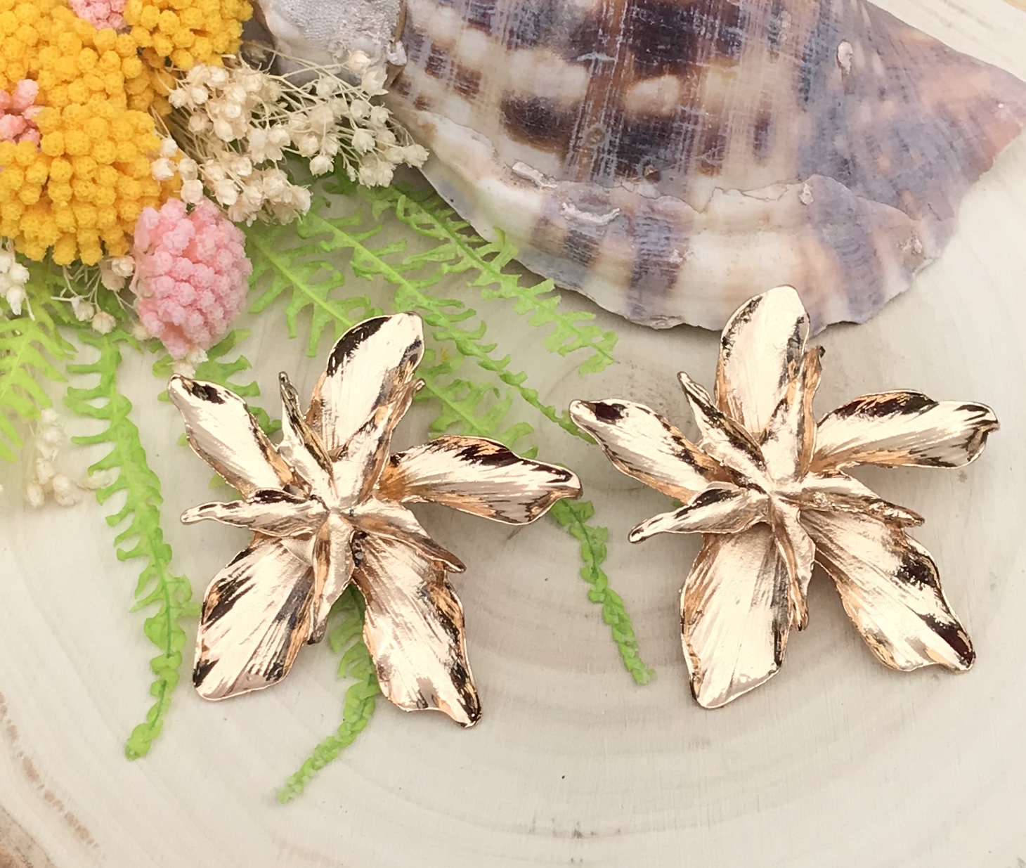 Brincos em forma de flores douradas envelhecidas com decoração natural ao fundo