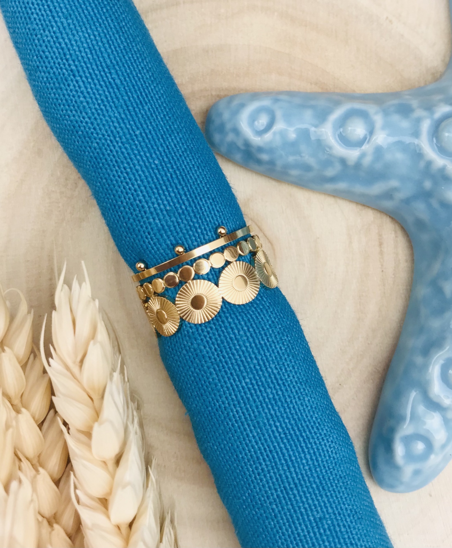 Anel dourado com discos em pano azul enrolado, estrela do mar cerâmica azul e espigas de trigo.