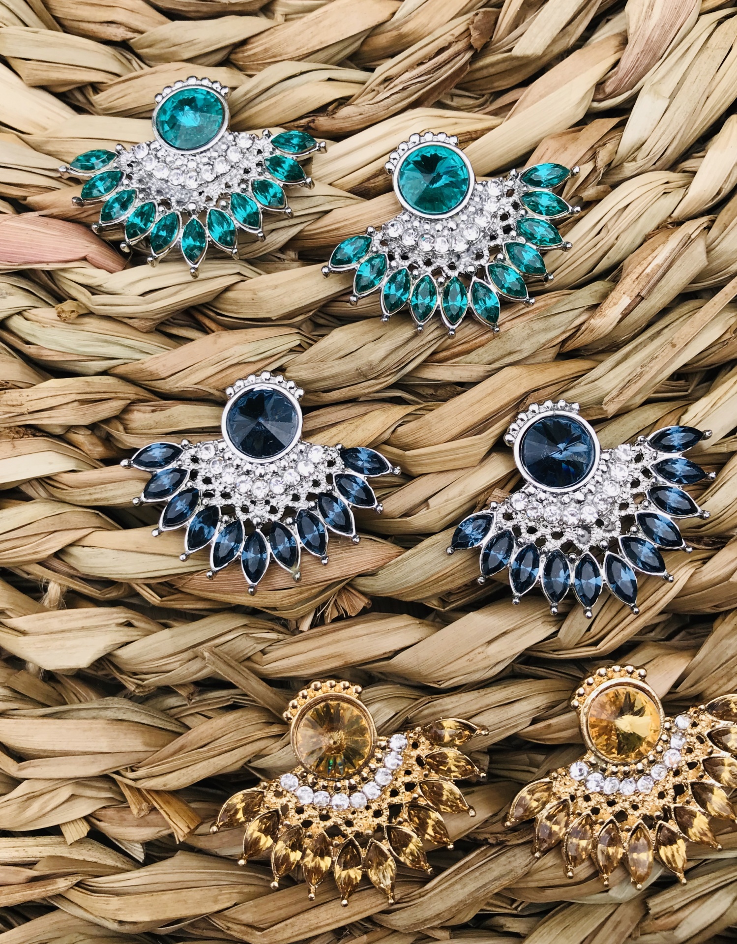 Brincos coloridos com pedras e detalhes metálicos sobre superfície de fibra natural