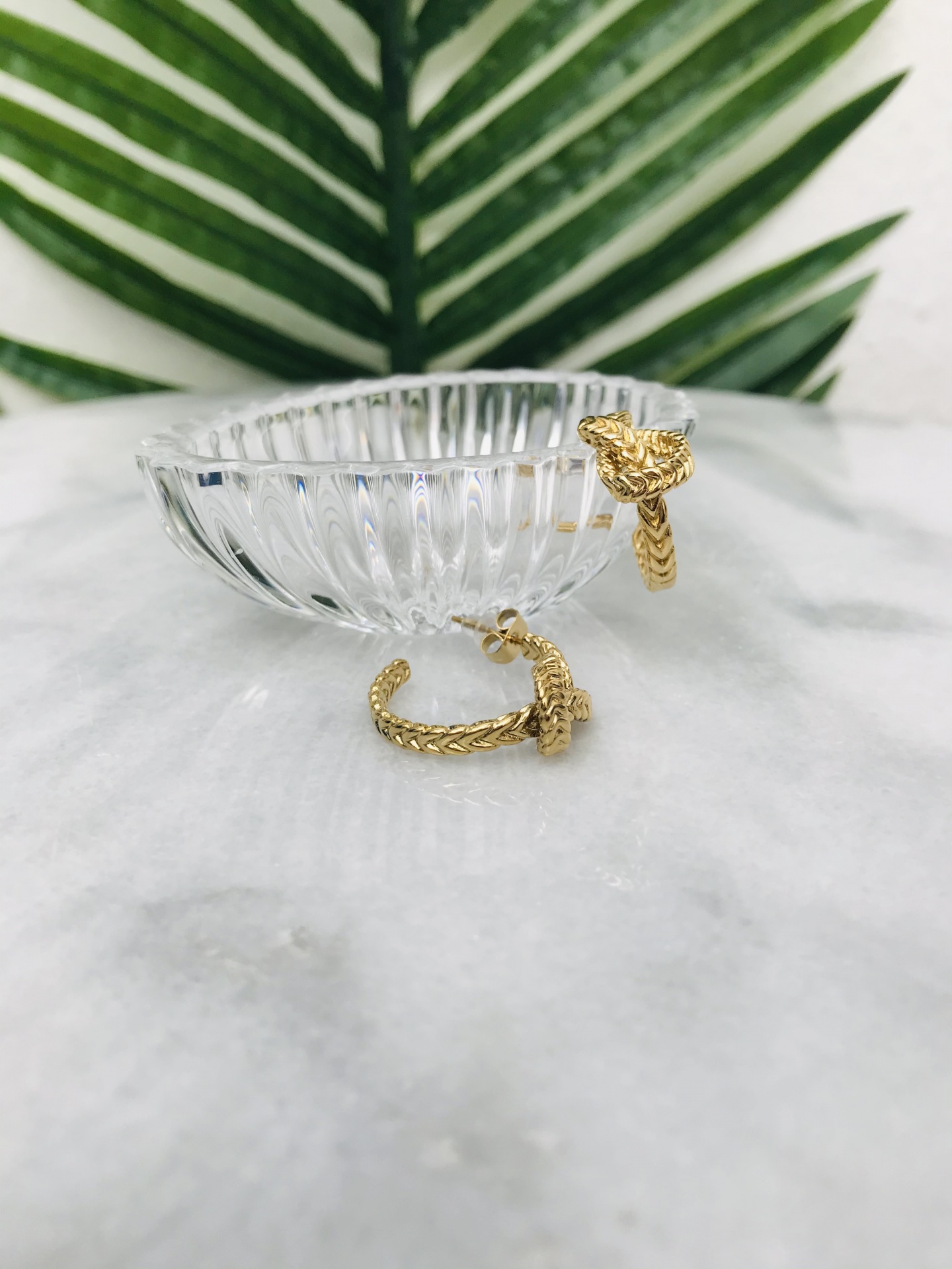 Brincos dourados com textura entrelaçada em prato de vidro transparente