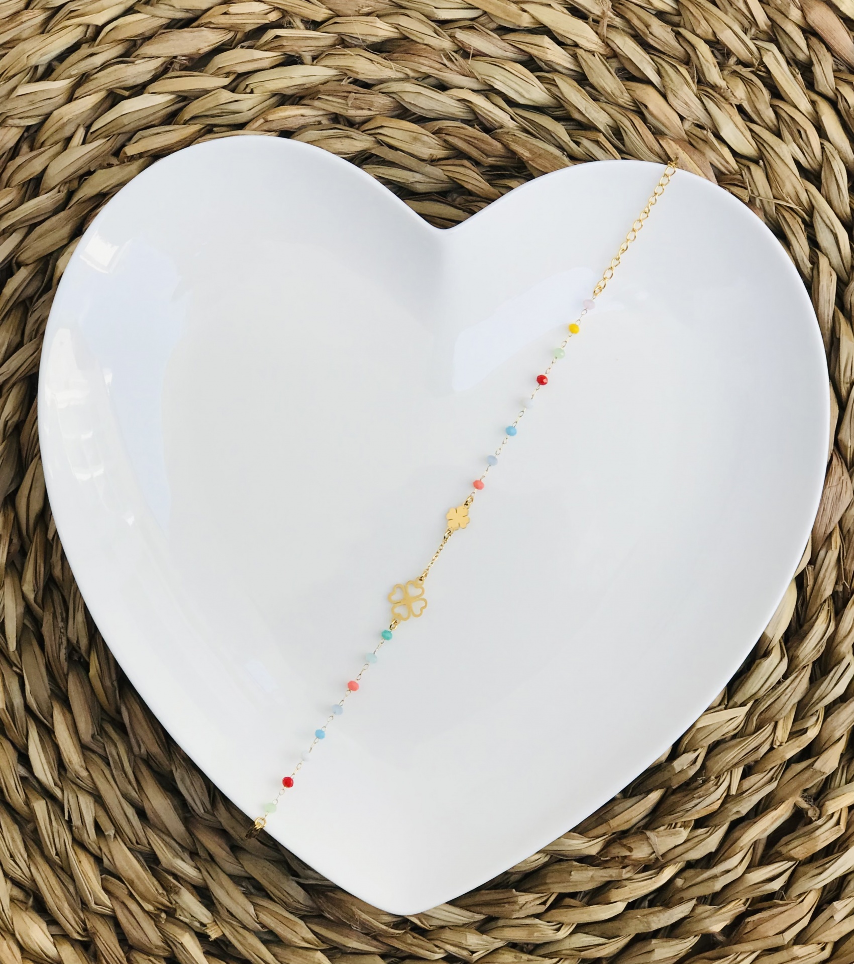 Pulseira dourada com contas coloridas sobre prato branco em forma de coração