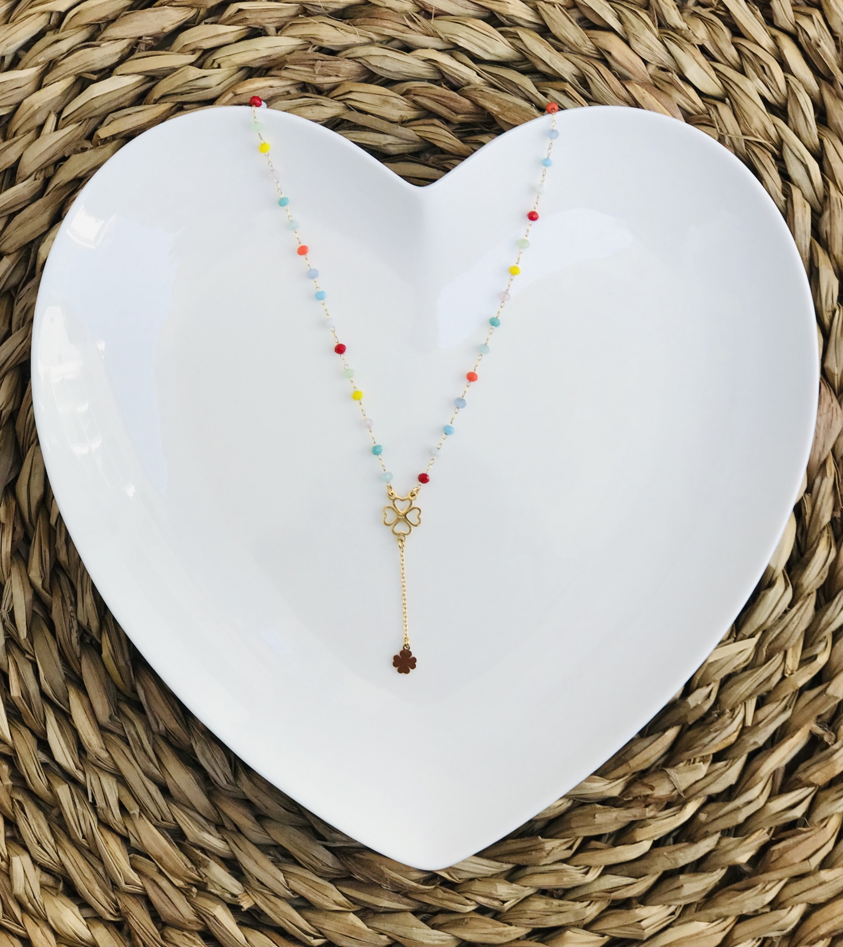 Colar com contas coloridas e pendente de flores sobre prato branco em forma de coração