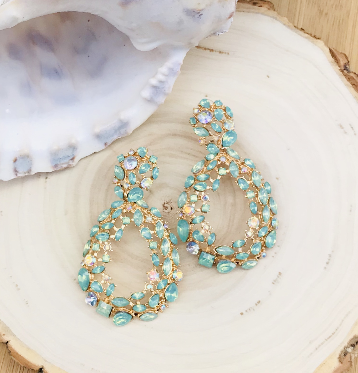 Brincos dourados com pedras turquesa em base de madeira com concha ao lado