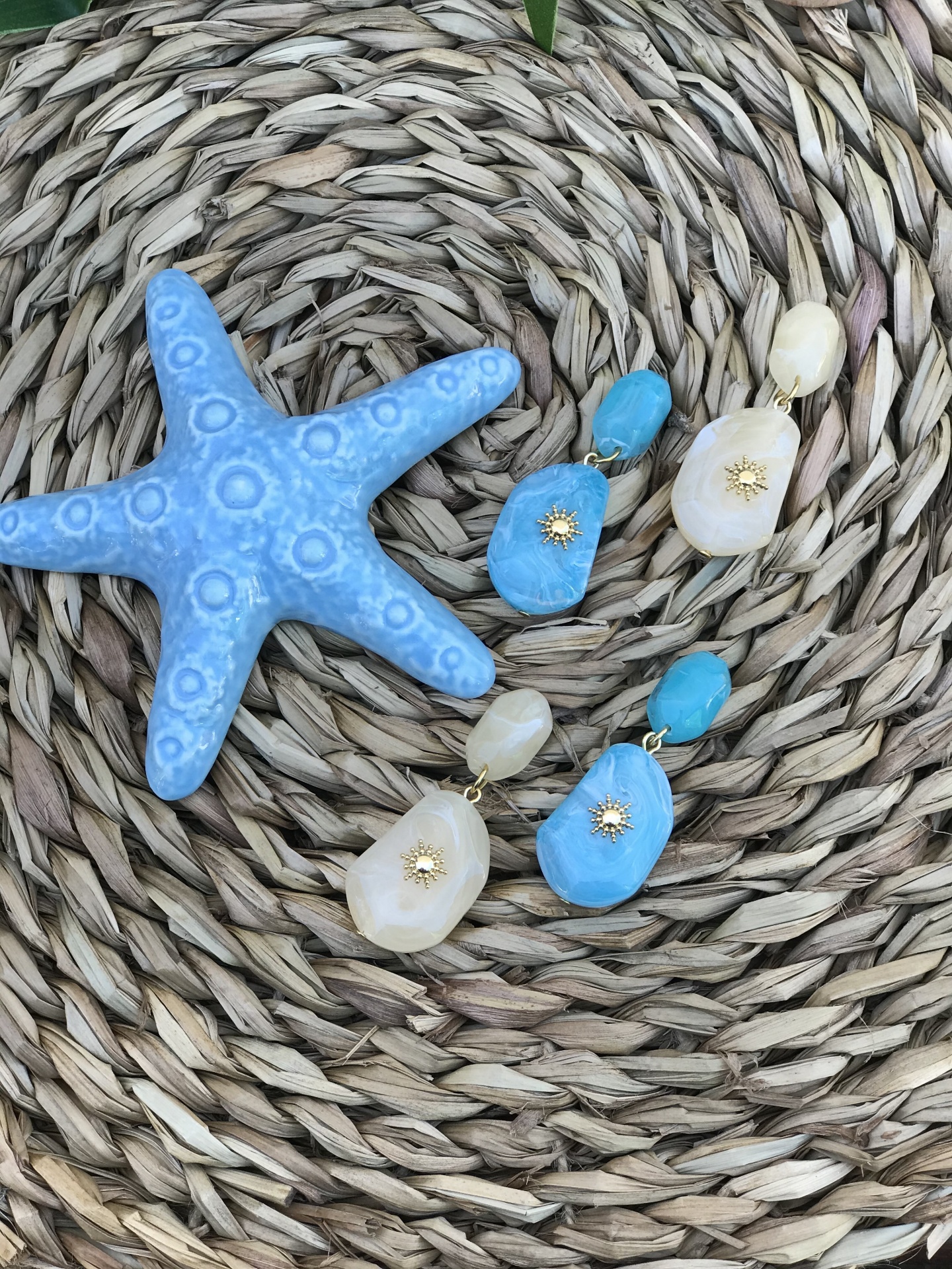 Brincos coloridos pendurados sobre superfície de fibra natural ao lado de uma estrela do mar azul