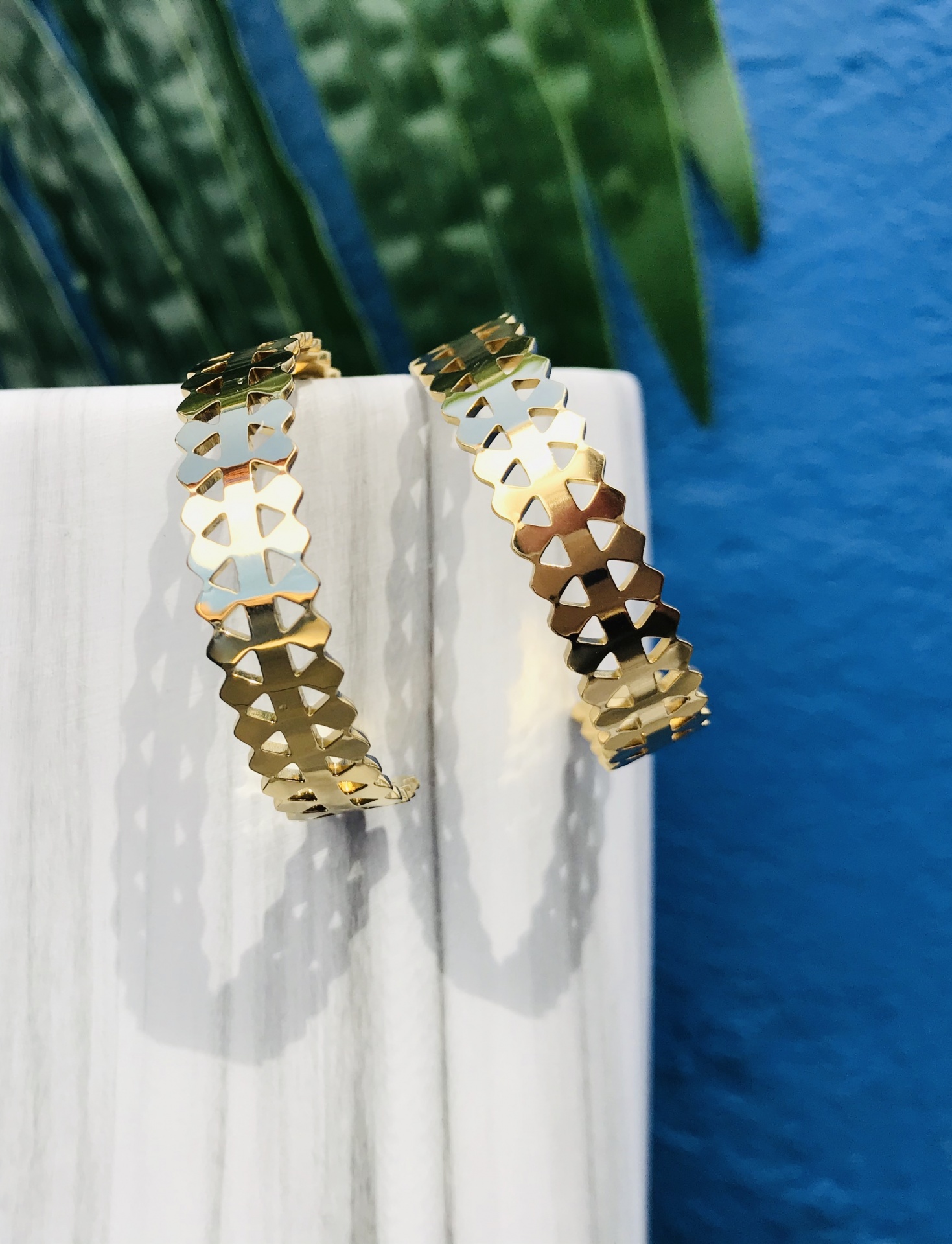 Brincos de argola dourados cortados em padrão recortado pendurados num suporte branco