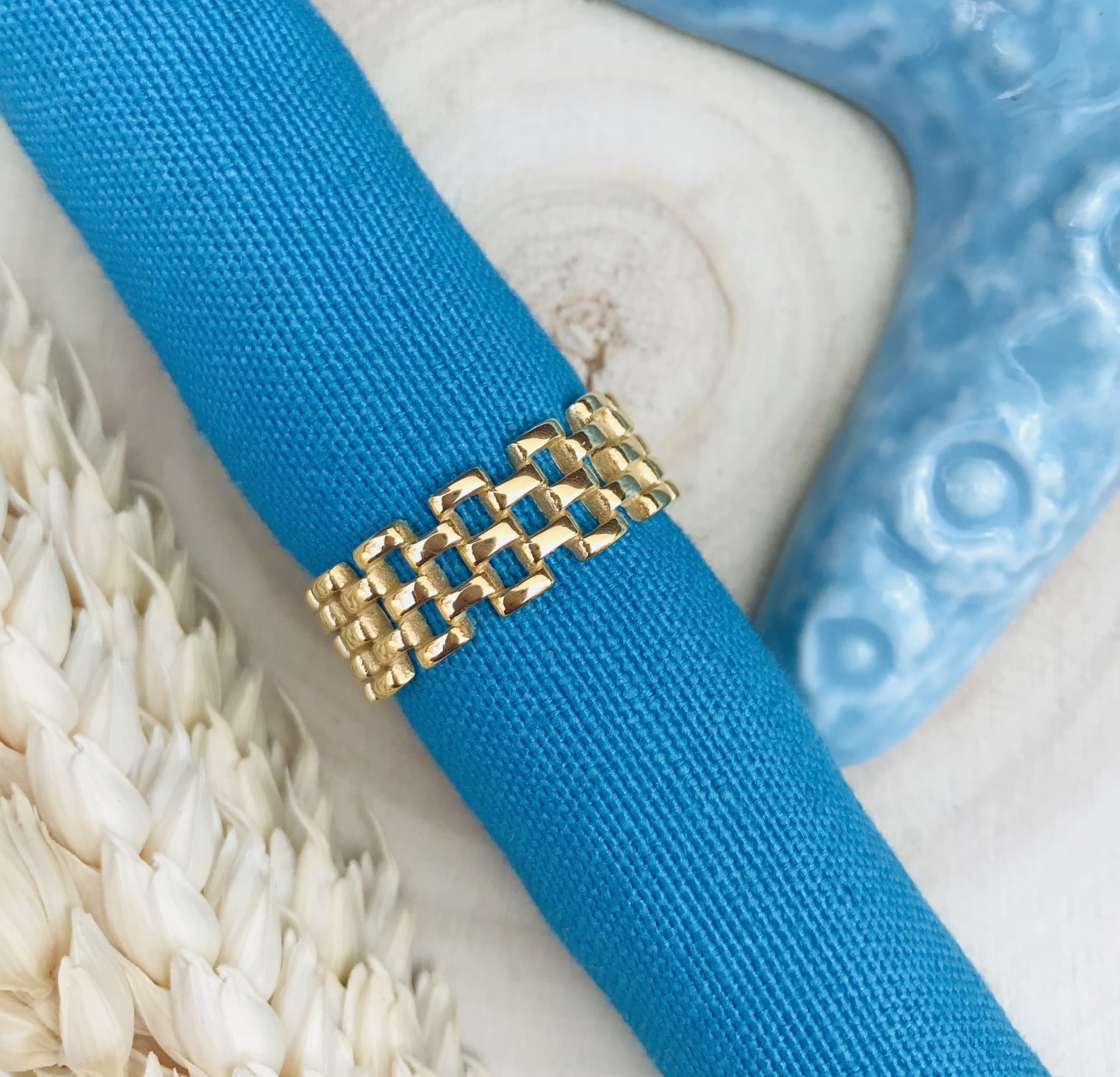 Anel dourado sobre tecido azul com fundo decorativo bege e azul