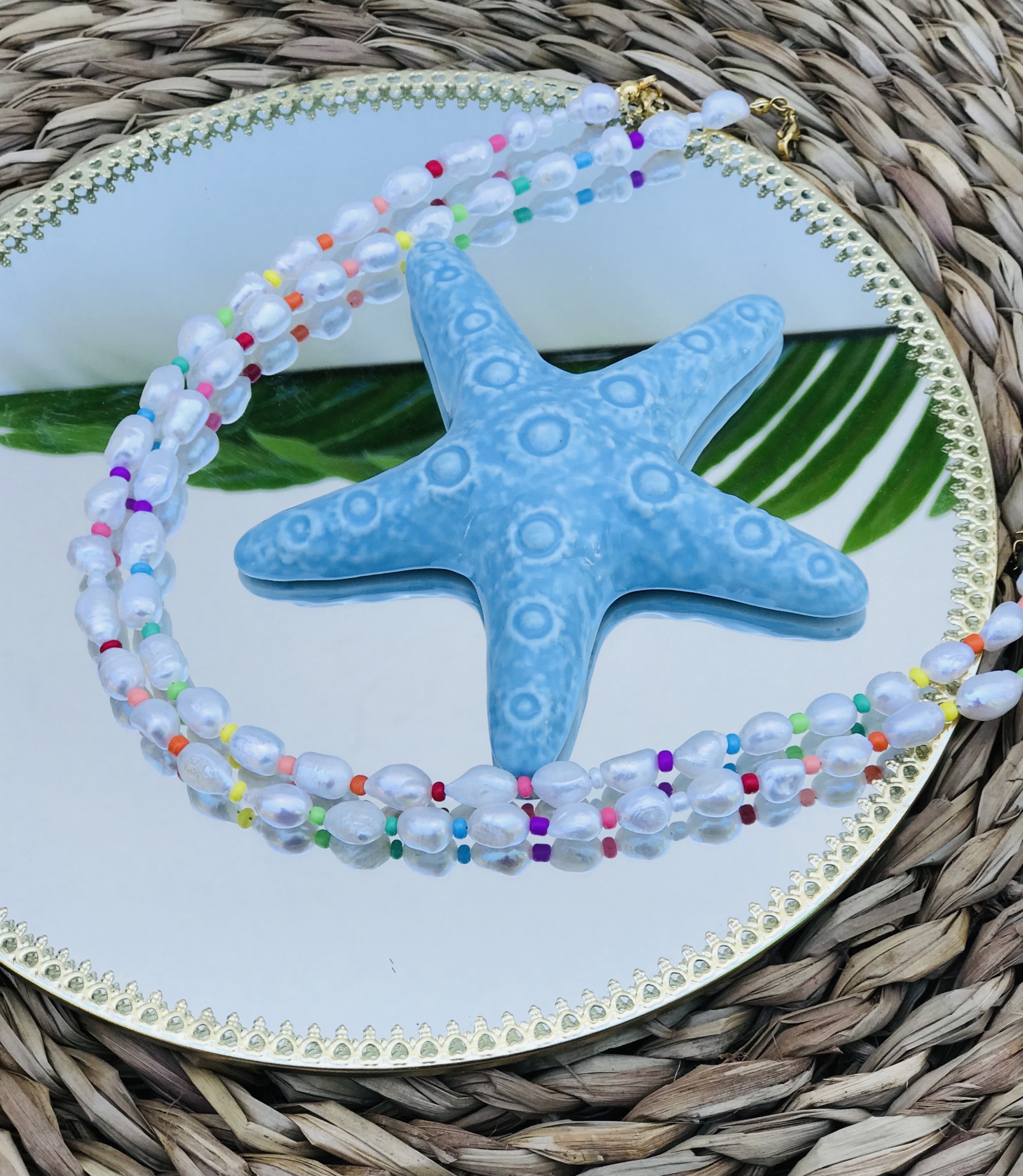 Colar de contas transparentes e coloridas com estrela do mar azul em espelho redondo