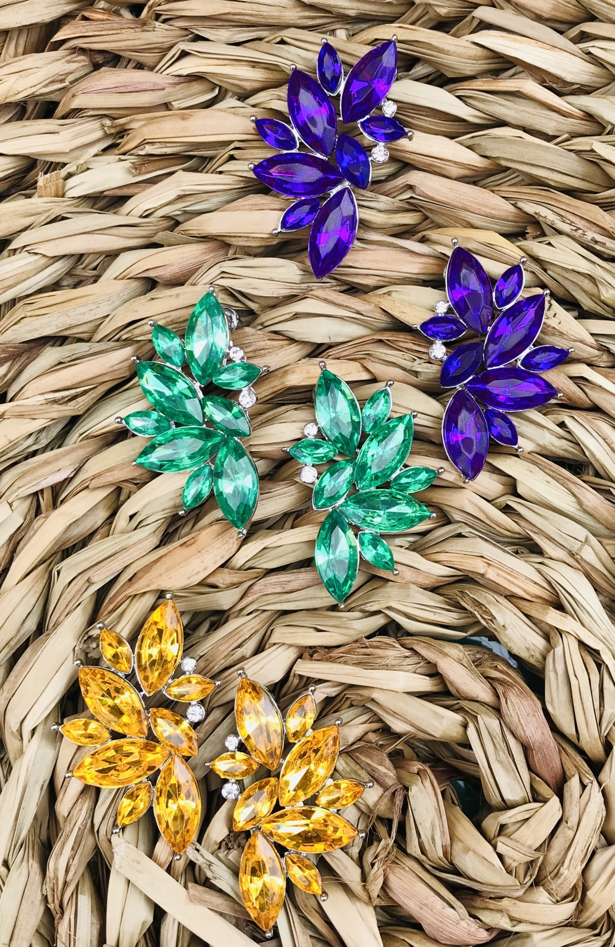 Brincos coloridos com pedras em forma de folhas sobre fundo de fibra entrelaçada