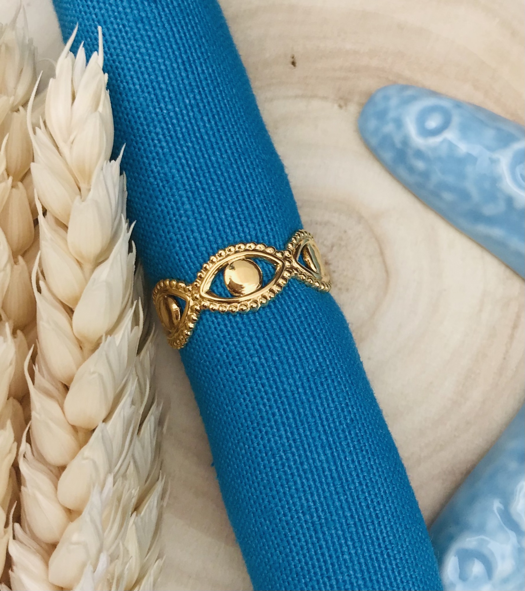 Anel dourado decorativo num tecido azul com espigas de trigo e cerâmica azul.
