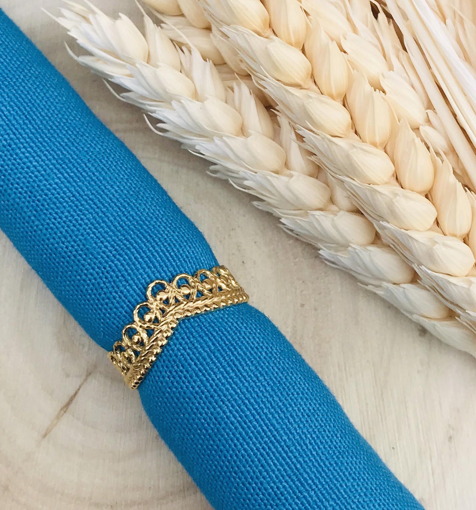 Guardanapo azul com argola dourada e espigas de trigo brancas sobre madeira
