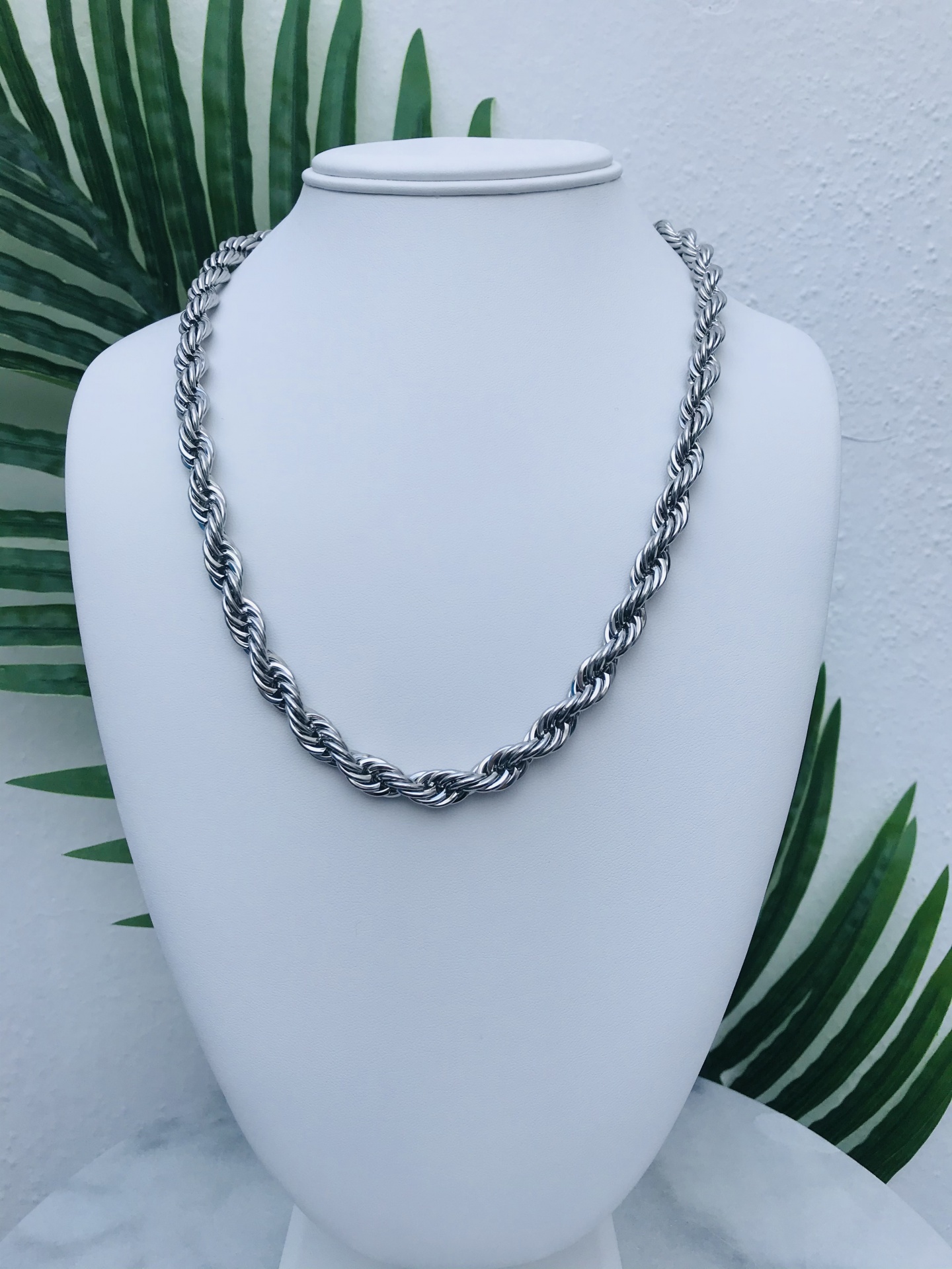 Colar de metal prateado com elos entrelaçados exposto em busto branco