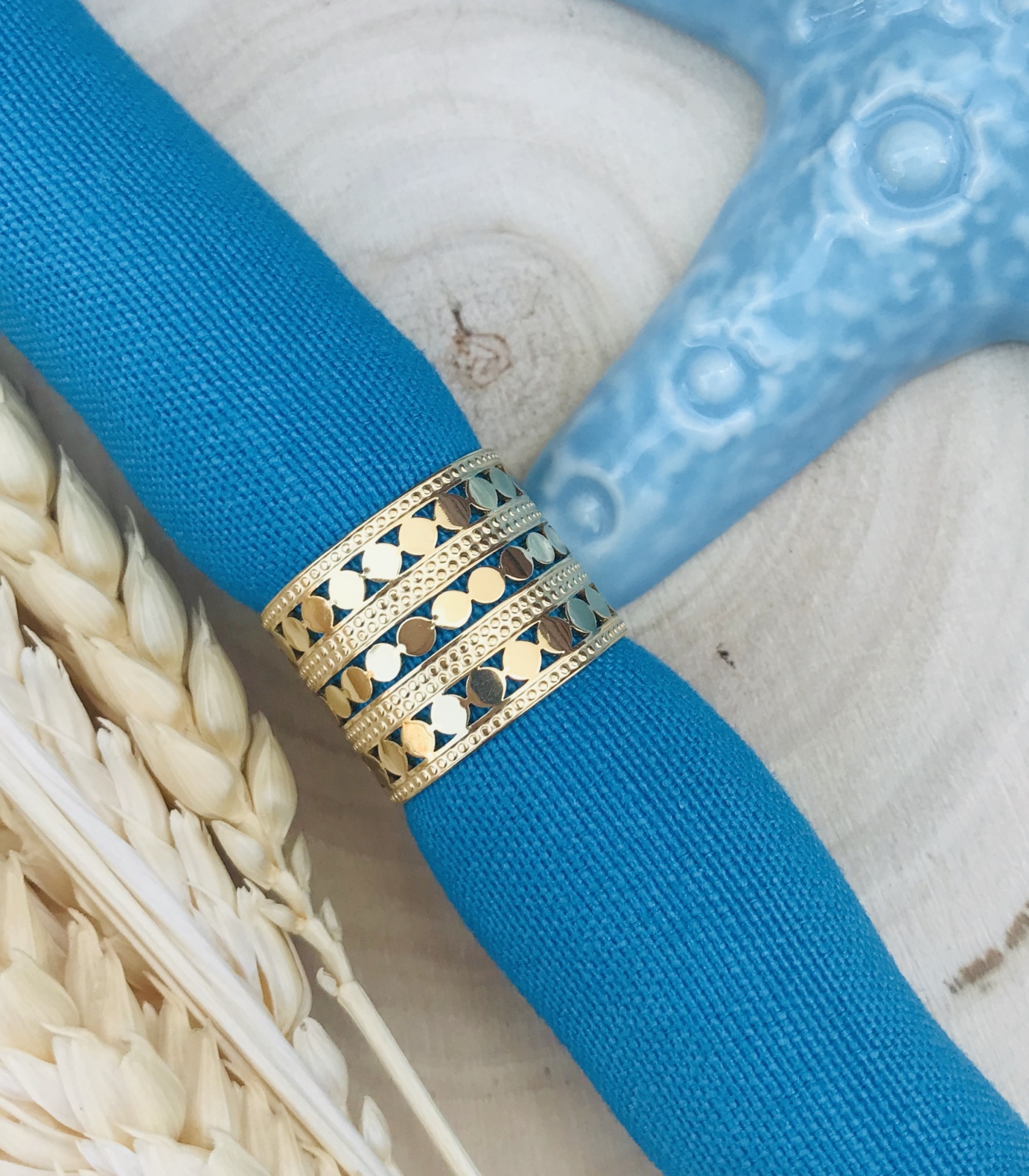 Guardanapo azul com argola decorativa dourada em base de madeira clara com ervas secas e objeto azul