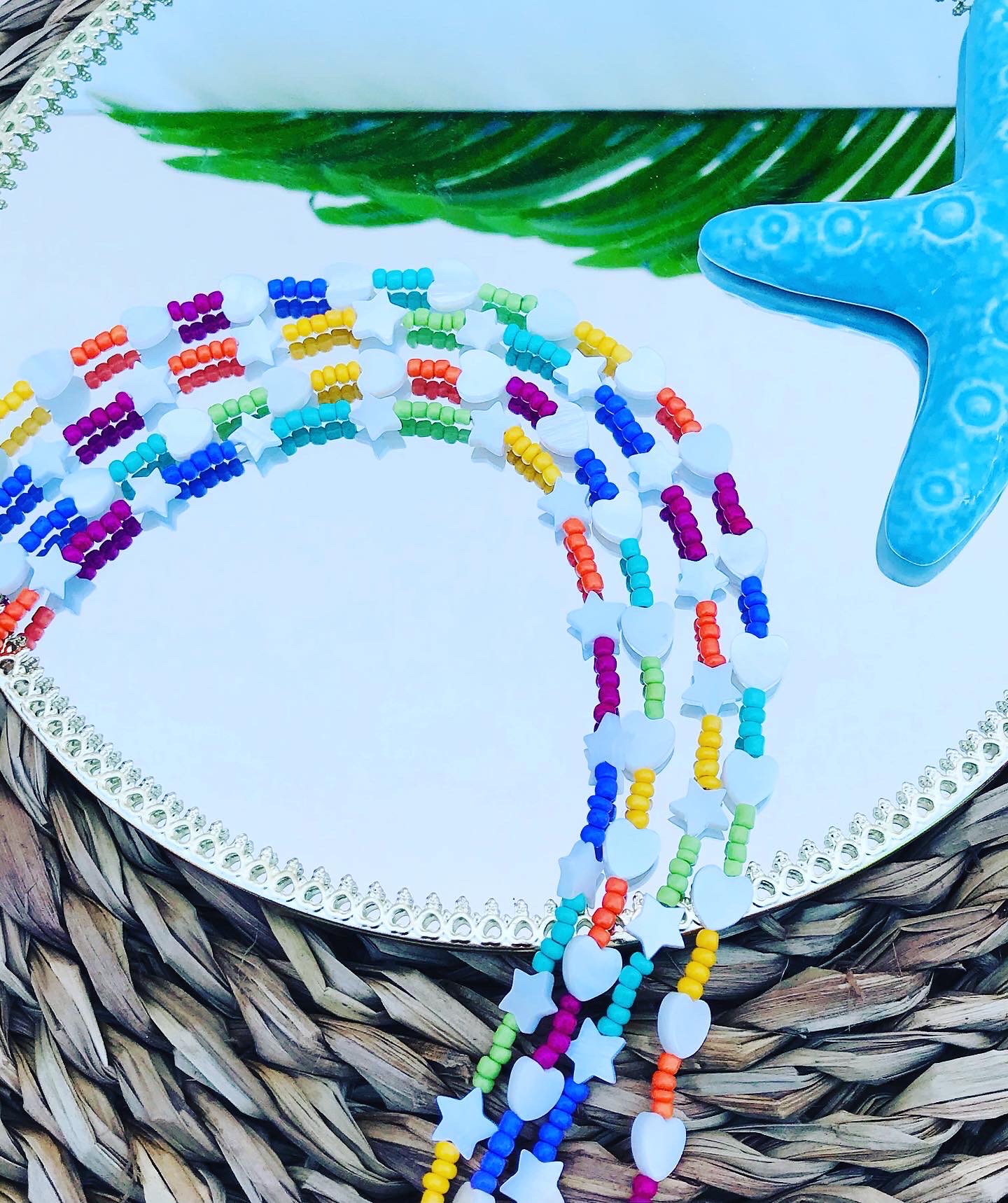 Colares coloridos em contas de plástico com formas variadas sobre espelho e estrela do mar azul