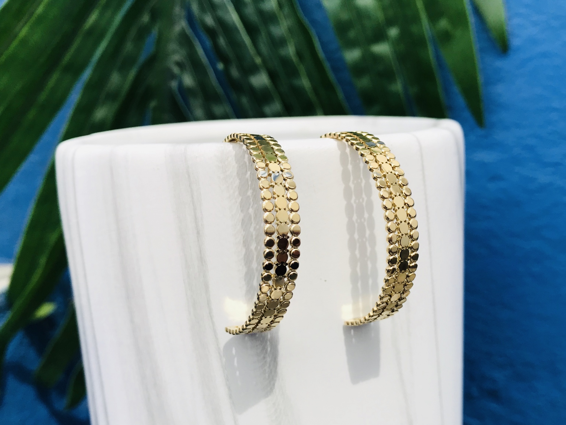 Brincos de argola dourados com padrão em relevo pendurados numa base branca