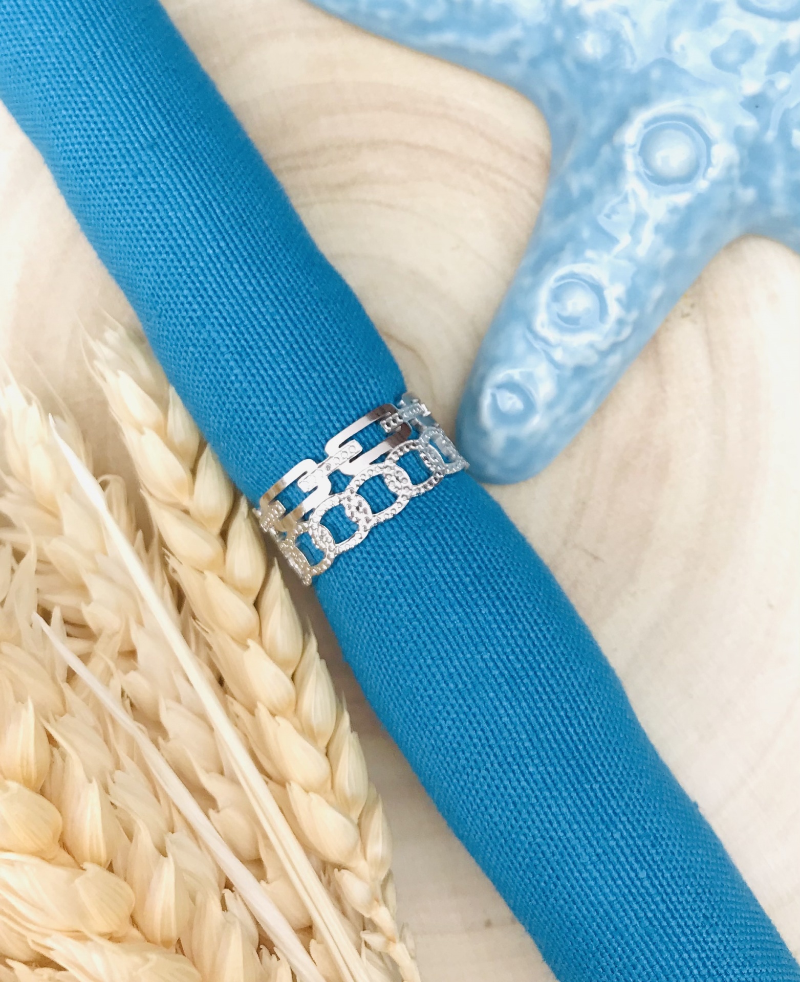 Argola de prata com padrão de elos em tecido azul, espigas secas e estrela-do-mar azul