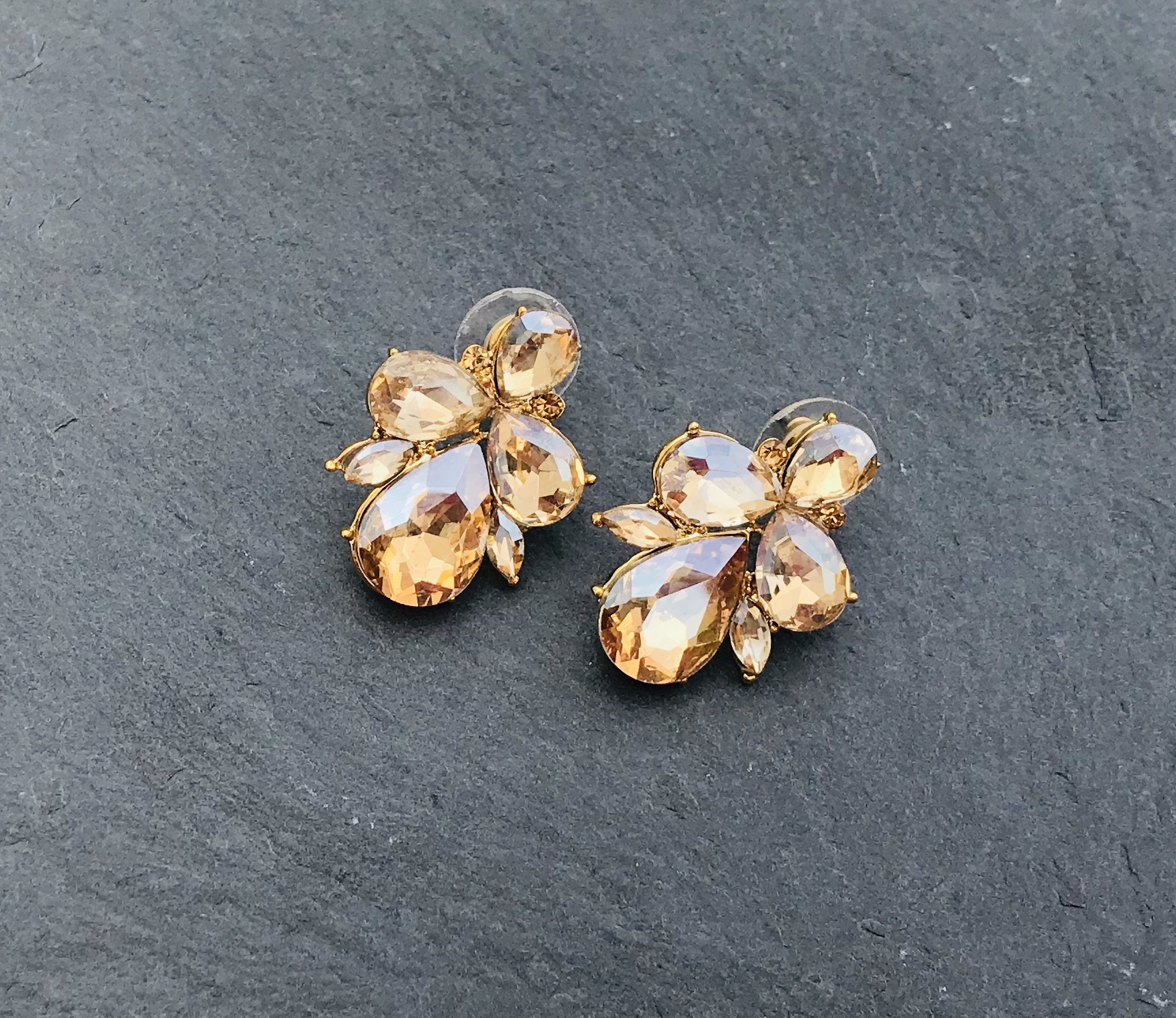 Brincos dourados com pedras âmbar sobre superfície de pedra cinza.