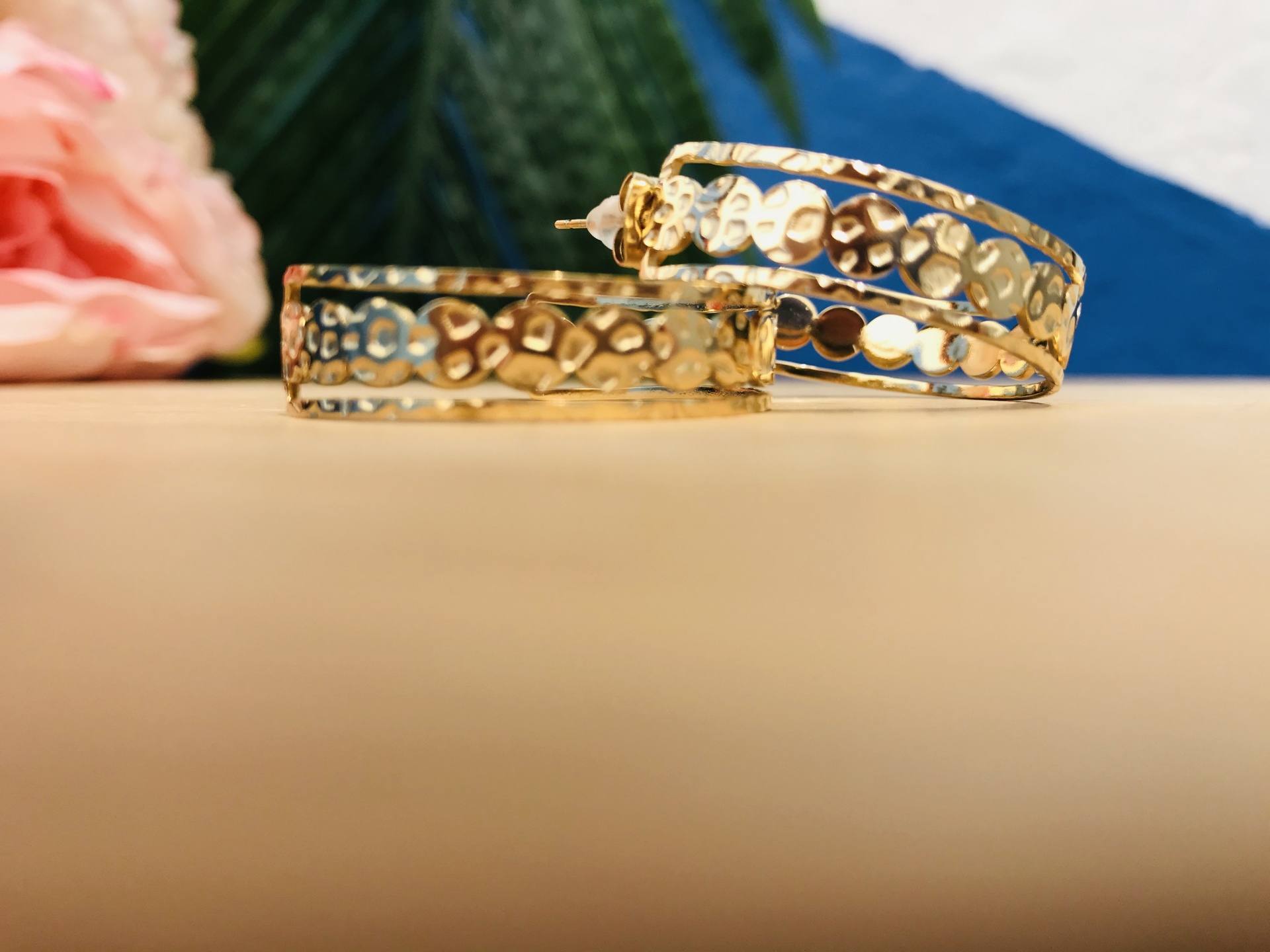 Par de brincos de argola texturizados dourados sobre superfície bege