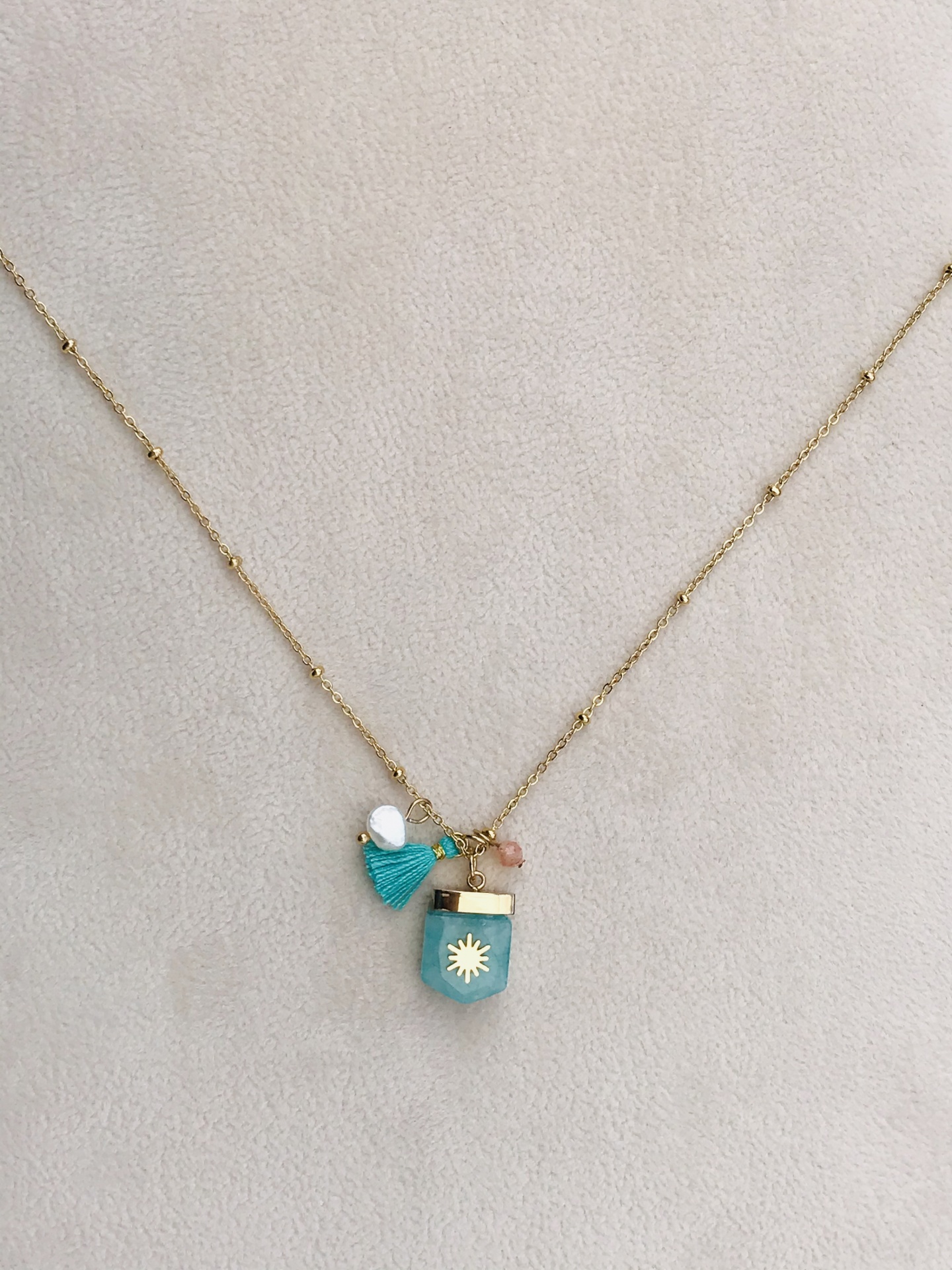 Colar dourado com pendentes coloridos sentado sobre fundo bege.