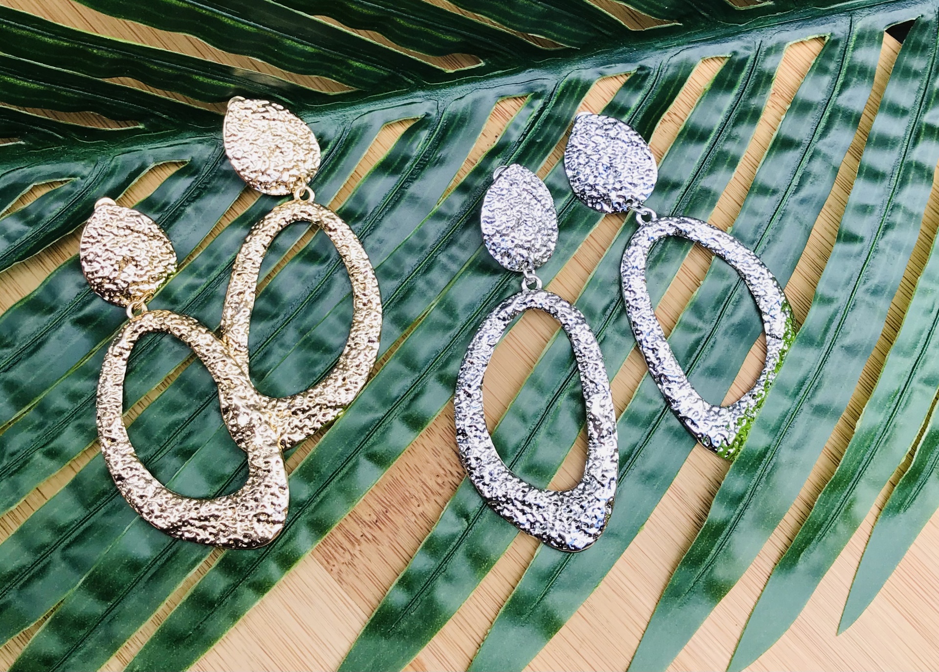 Dois pares de brincos texturizados, dourado e prateado, sobre folhas verdes