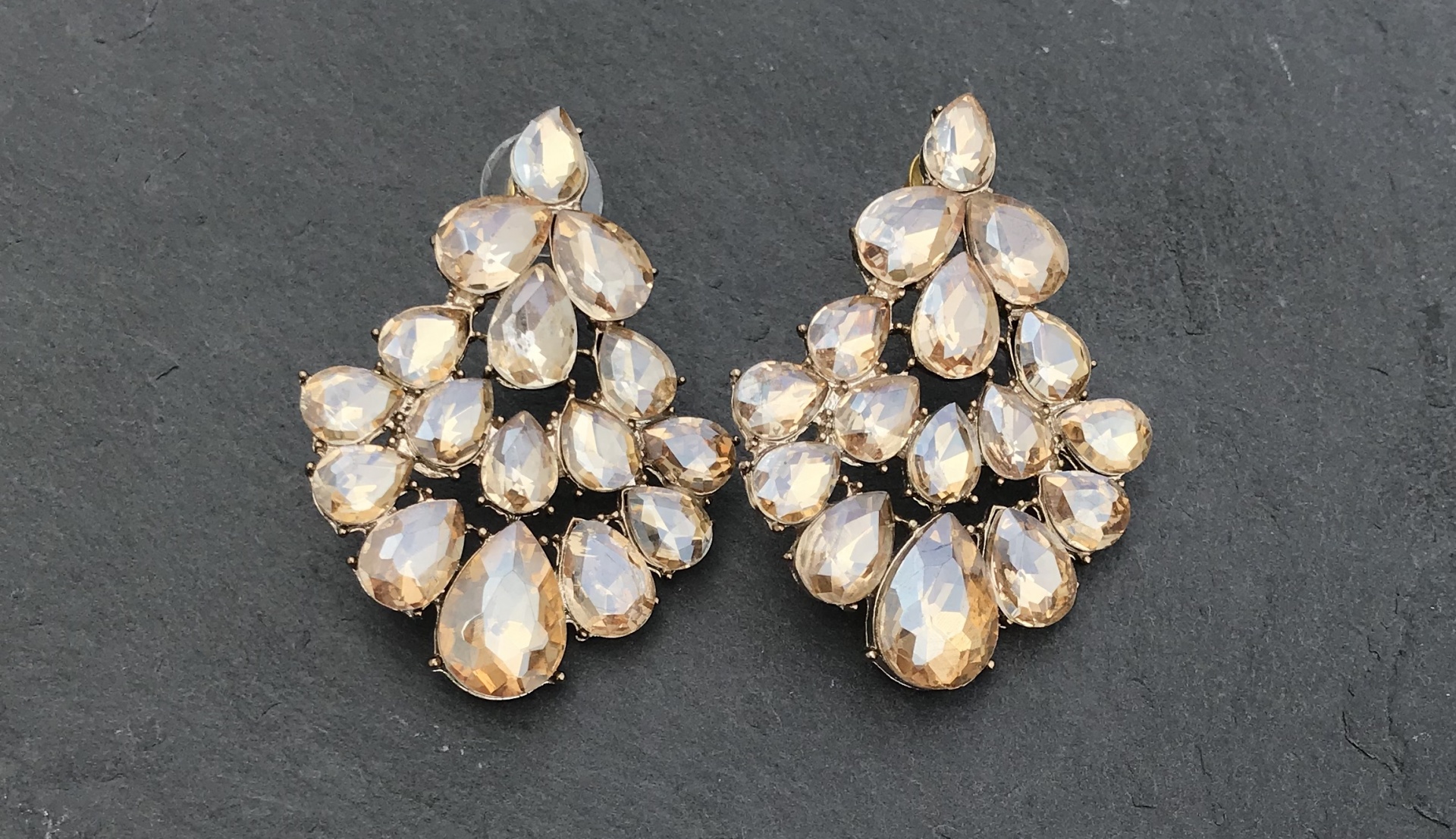 Brincos com pedras brilhantes bege e dourado em fundo preto