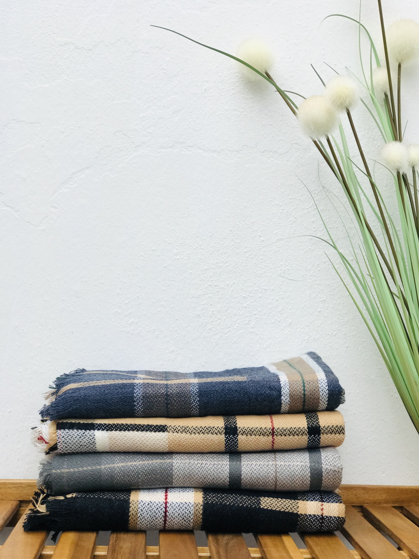 Quatro mantas ou lenços xadrez empilhados sobre superfície de madeira com ramos decorativos