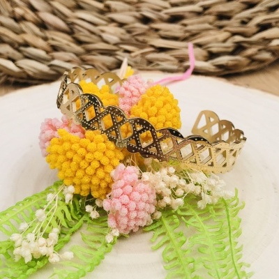 Pulseira dourada com flores decorativas amarelas e rosa sobre prato branco