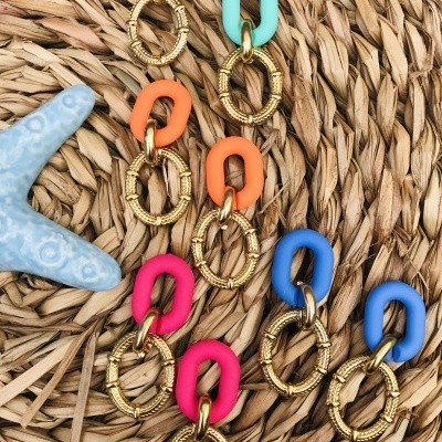 Brincos coloridos com argolas de resina e douradas sobre tapete de palha com estrela do mar azul