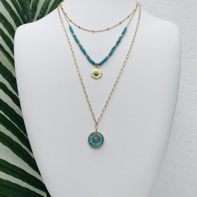 Colar triplo dourado com detalhes azul-turquesa exibido em busto branco