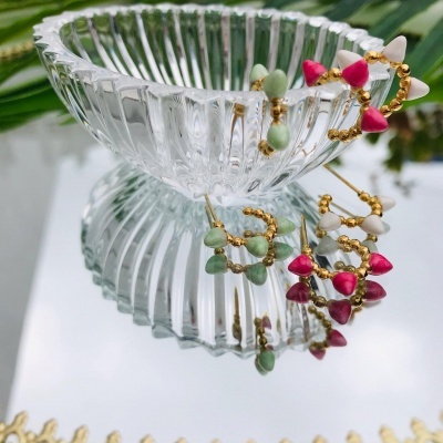 Brincos de argola coloridos sobre taça de vidro e espelho com moldura dourada