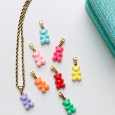 Colar dourado com pendente ursinho lilás e vários pendentes coloridos ao lado sobre fundo branco