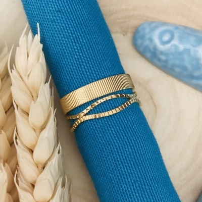 Anel dourado de três bandas sobre tecido azul com espigas secas ao lado
